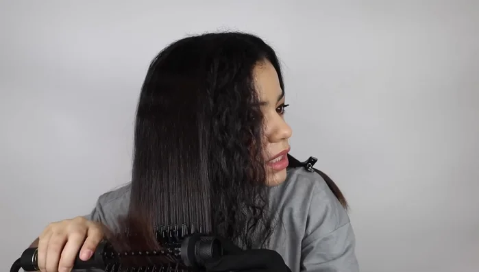Woman blow-drying curly hair straight.